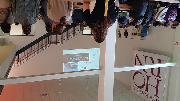 Foto des Vortrags in der Mensa der Schule mit Rücken von Schülern und weiter hinten der Vortrag an der Wand per Beamer projiziert