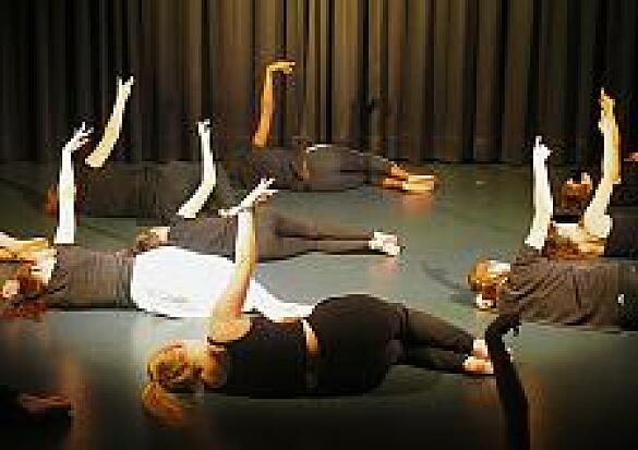 Foto von Schülern auf dem Boden auf der Bühne mit Händen nach oben