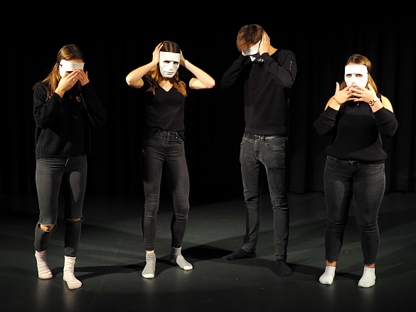 Foto von 4 Schülern in schwarz mit weißen MAsken auf der Bühne