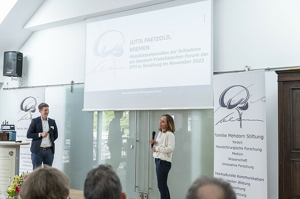 Foto der Rede vor einer Leinwand mit Rednerpult und Publikum