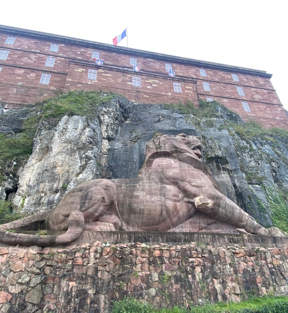 Foto einer Wandmauer mit einem eingehauenen Löwen, darüber ein Schloss oder so